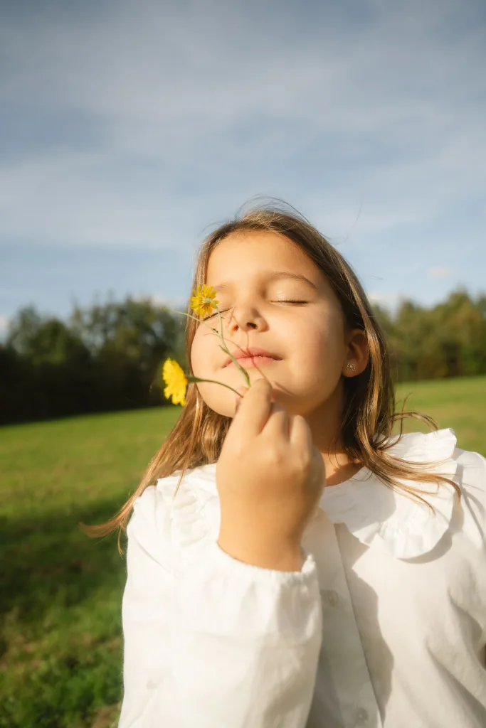 Meisje met gesloten ogen houdt een gele bloem bij haar gezicht