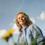 Vrouw kijkt glimlachend omhoog in de zon tussen bloemen