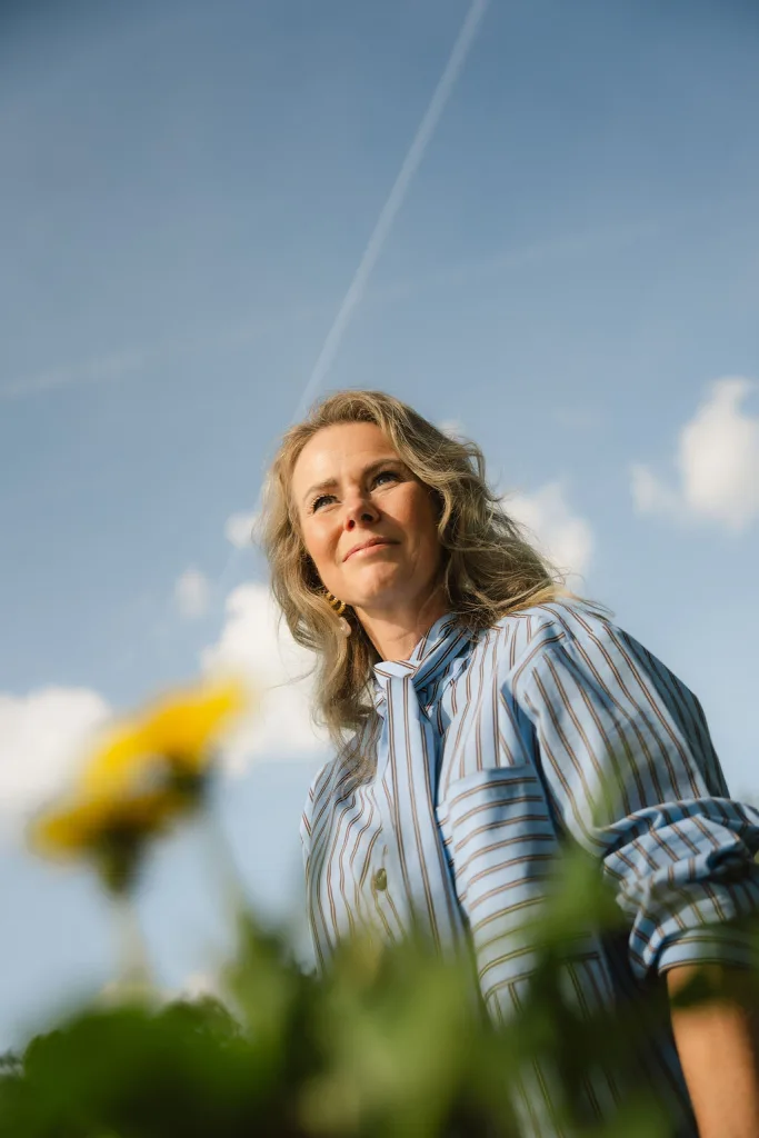 Vrouw kijkt glimlachend omhoog in de zon tussen bloemen